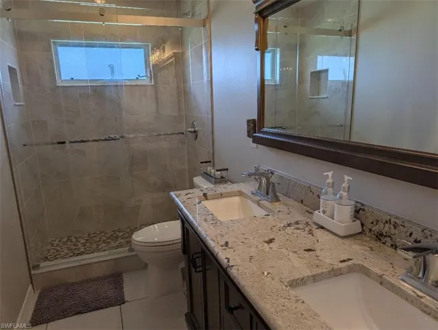 Bathroom with toilet, a shower stall, double vanity, and tile patterned floors