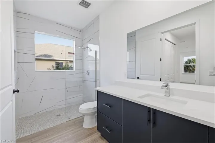 Contemporary bathroom featuring a dark gray vanity with a white countertop and an integrated sink, polished chrome faucet, and a large wall-mounted mirror