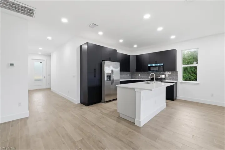 Open-concept kitchen featuring dark cabinetry, stainless steel appliances, a center island with a white countertop, and wood-finish flooring