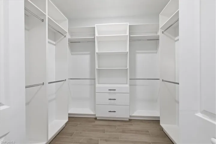 Walk-in closet featuring built-in white shelving, integrated drawers with black hardware, chrome hanging rods, and wood-look plank flooring