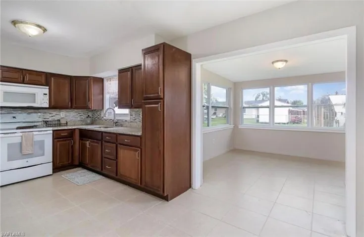 Kitchen featuring white appliances, dark brown cabinetry, backsplash, light stone counters, and light tile patterned flooring