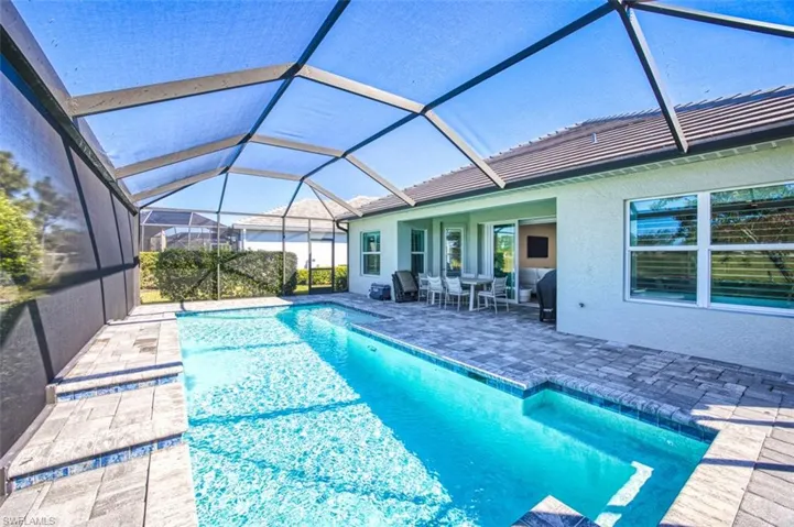 Outdoor pool with a sunroom, a patio, glass enclosure, and outdoor dining space