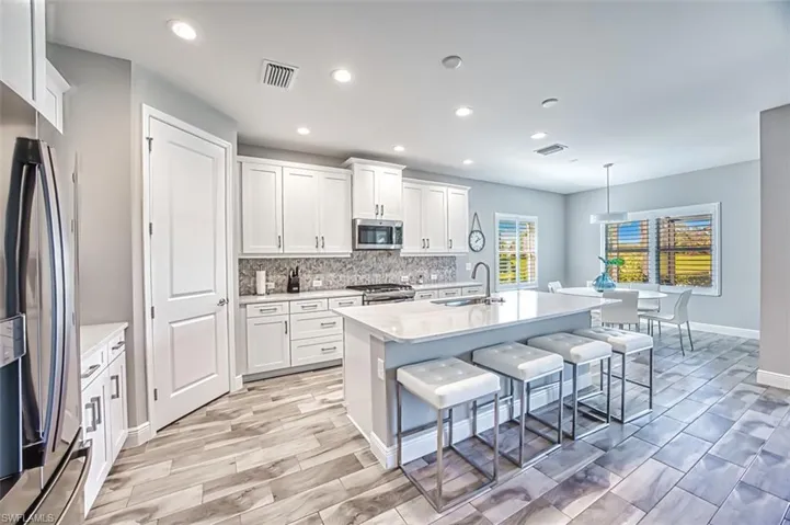 Kitchen featuring stainless steel appliances, an island with sink, pendant lighting, white cabinetry, and light stone counters
