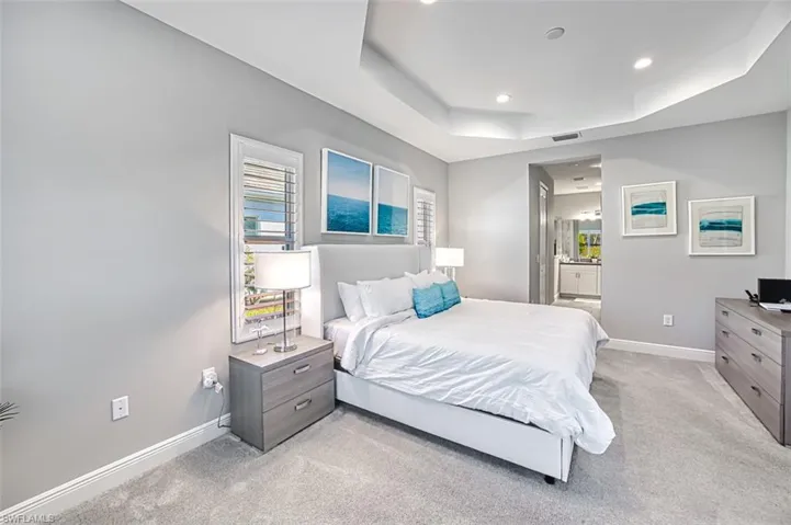 Bedroom with light carpet, a raised ceiling, ensuite bath, and recessed lighting