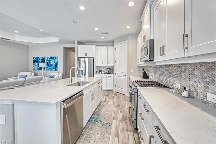 Kitchen featuring stainless steel appliances, light stone countertops, white cabinets, open floor plan, and recessed lighting