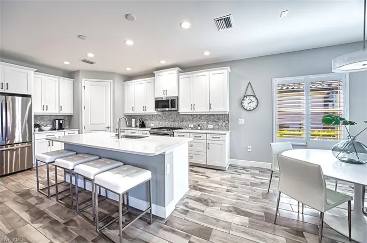 Kitchen featuring stainless steel appliances, white cabinets, wood finish floors, and a kitchen breakfast bar