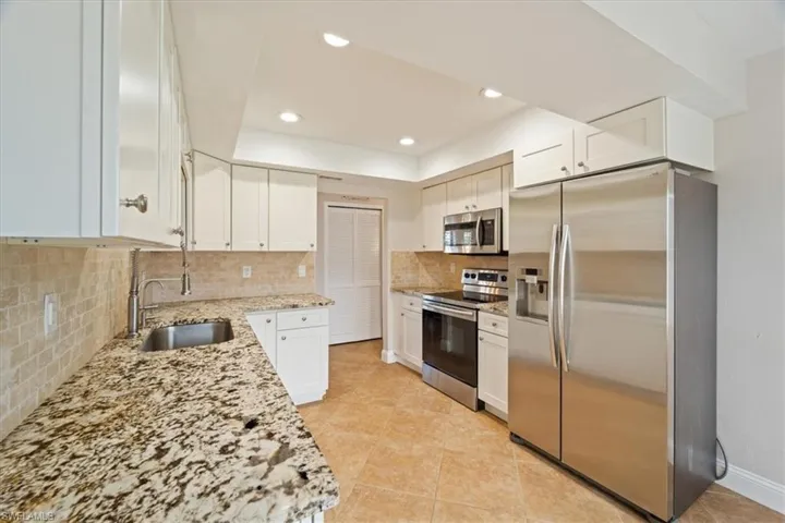 Kitchen featuring light tile patterned flooring, white cabinetry, tasteful backsplash, stainless steel appliances, and light stone countertops