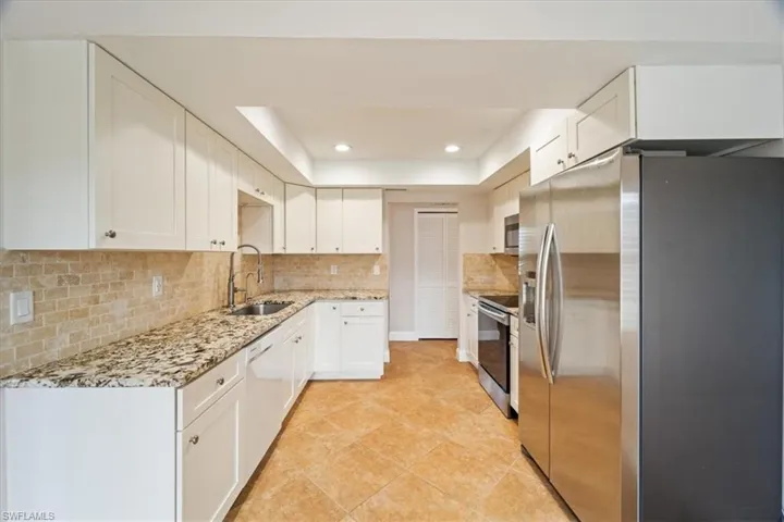 Kitchen featuring stainless steel appliances, sink, light tile patterned floors, decorative backsplash, and white cabinetry