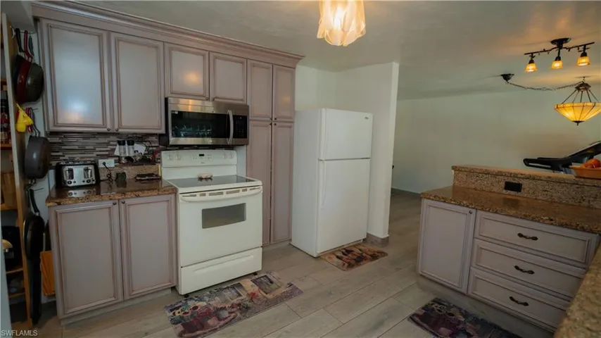 Kitchen featuring light hardwood / wood-style flooring, dark stone counters, white appliances, and tasteful backsplash