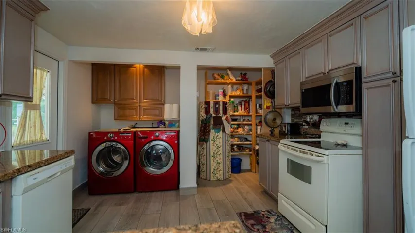Kitchen with dark stone counters, white appliances, light wood-type flooring, and washing machine and dryer
