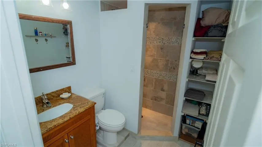 Bathroom featuring tiled shower, tile flooring, vanity, and toilet