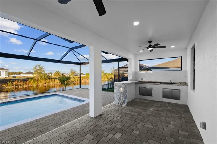 View of pool with glass enclosure, a water view, sink, ceiling fan, and a patio area