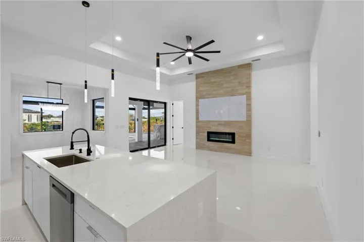 Kitchen with white cabinetry, sink, stainless steel dishwasher, decorative light fixtures, and a center island with sink