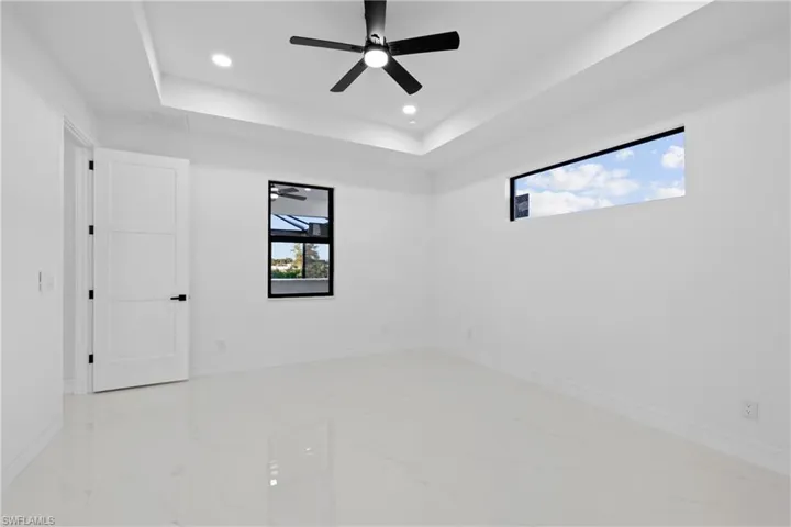 Empty room with a tray ceiling, a wealth of natural light, and ceiling fan