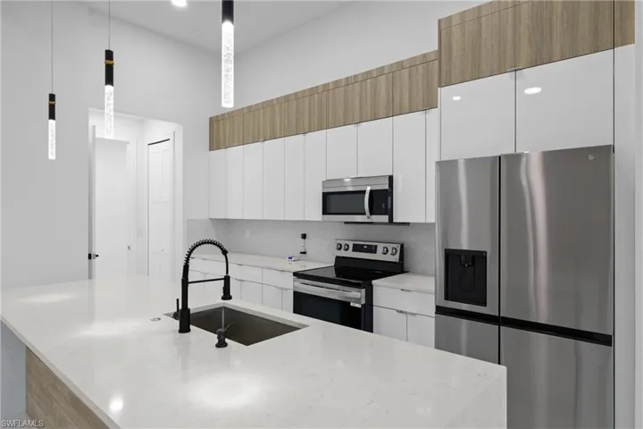 Kitchen with light stone countertops, appliances with stainless steel finishes, sink, white cabinets, and hanging light fixtures