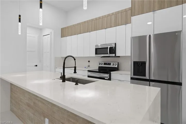 Kitchen with hanging light fixtures, sink, white cabinets, and stainless steel appliances
