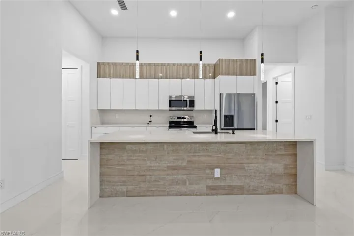 Kitchen featuring white cabinets, sink, stainless steel appliances, and an island with sink