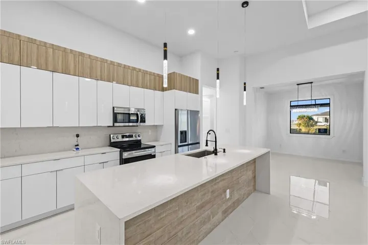 Kitchen featuring white cabinetry, sink, pendant lighting, a kitchen island with sink, and appliances with stainless steel finishes