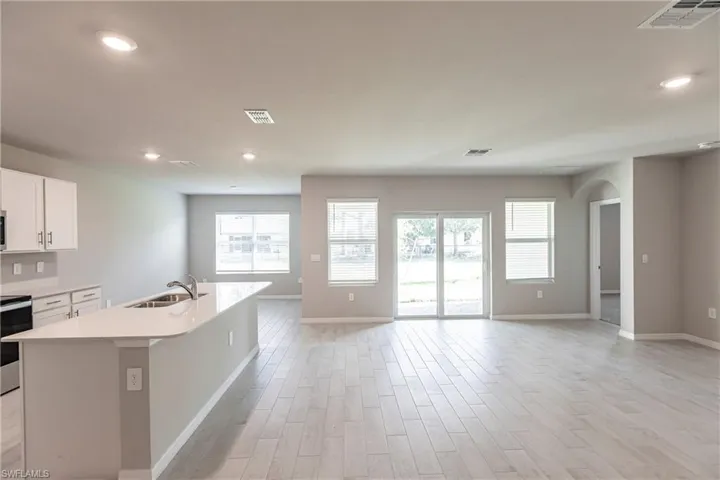 Kitchen with range, white cabinetry, light hardwood / wood-style flooring, sink, and a center island with sink