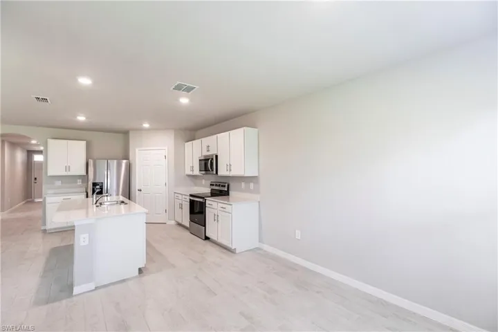 Kitchen with appliances with stainless steel finishes, white cabinets, sink, a kitchen island with sink, and light wood-type flooring