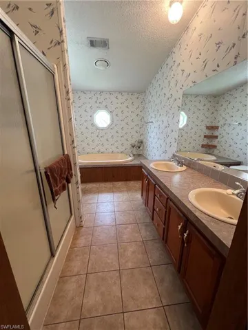 Full bath with a textured ceiling, a bath, a stall shower, double vanity, and tile patterned flooring