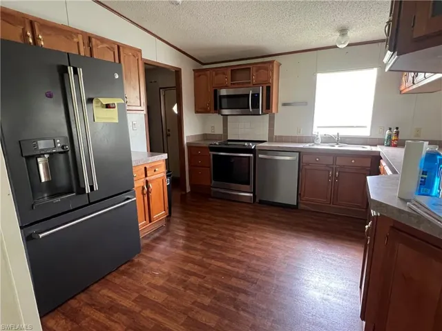 Kitchen with ornamental molding, appliances with stainless steel finishes, a textured ceiling, dark wood-style floors, and lofted ceiling