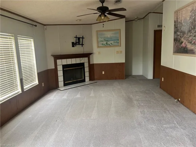 Unfurnished living room with wood walls, wainscoting, a ceiling fan, a textured ceiling, and carpet flooring