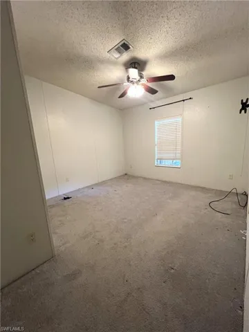 Spare room featuring a textured ceiling, ceiling fan, and carpet floors