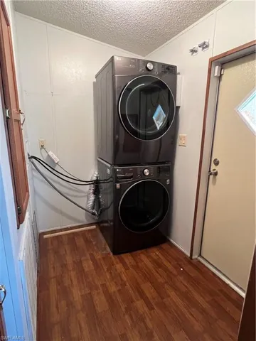 Washroom with stacked washing machine and dryer, a textured ceiling, wood finished floors, and crown molding