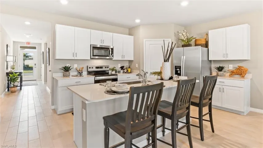 Model Home. The kitchen features white cabinetry, stainless steel appliances, and an island with seating
