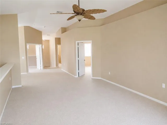 Spacious living room with neutral-toned carpeting and walls, featuring a decorative ceiling fan.