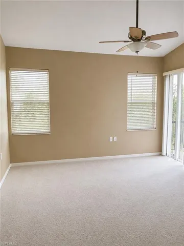 Spacious room featuring neutral carpeting, a ceiling fan with integrated lighting, two windows with blinds, and a sliding glass door