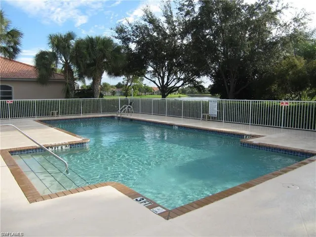 Fenced swimming pool with integrated steps, concrete deck, and perimeter brick coping