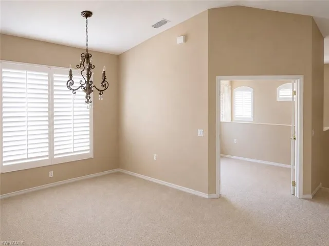 Room with vaulted ceiling, featuring a decorative chandelier and neutral-toned carpet flooring
