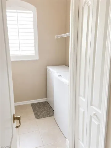 Dedicated laundry area featuring ceramic tile flooring, a built-in wire shelf, and an arched window with plantation shutters