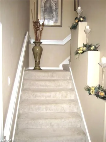 Carpeted staircase featuring a white handrail and crown molding details