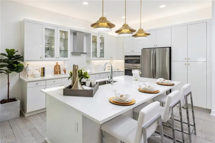 Kitchen with wall chimney range hood, appliances with stainless steel finishes, an island with sink, and light wood-type flooring
