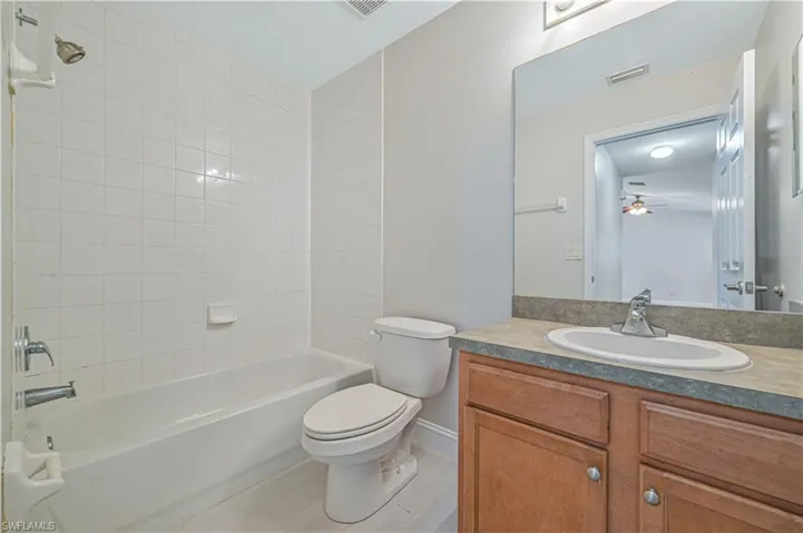 Full bathroom featuring tiled shower / bath, tile flooring, vanity with extensive cabinet space, and toilet