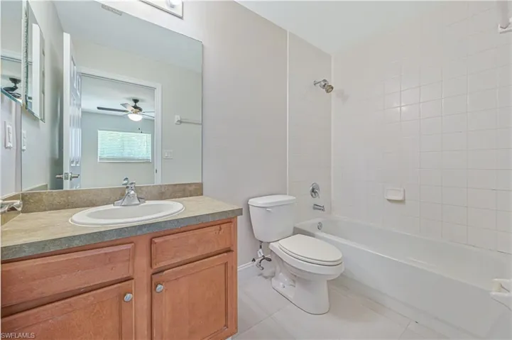 Full bathroom featuring tile flooring, tiled shower / bath, oversized vanity, ceiling fan, and toilet