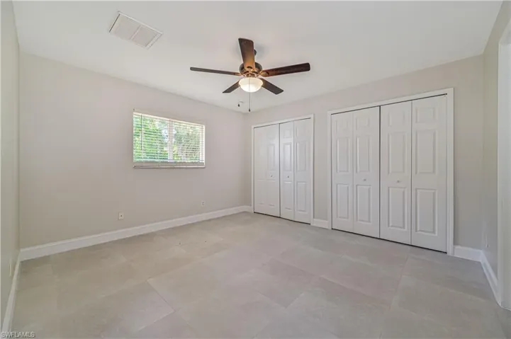 Unfurnished bedroom with two closets, ceiling fan, and light tile floors