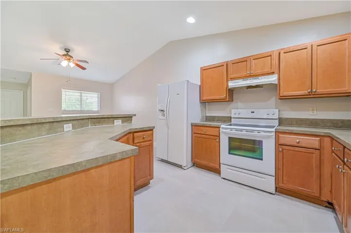 Kitchen featuring white appliances, vaulted ceiling, ceiling fan, and light tile floors
