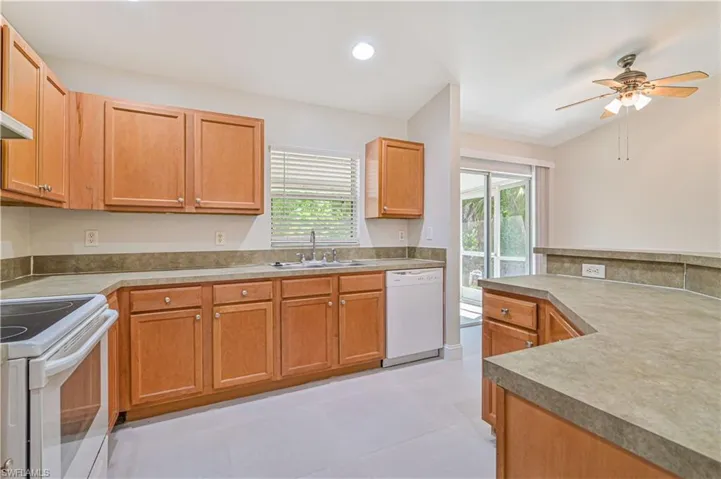 Kitchen featuring ceiling fan, white appliances, vaulted ceiling, light tile flooring, and sink