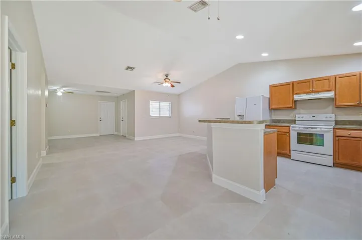 Kitchen with light tile flooring, ceiling fan, a center island, white appliances, and lofted ceiling