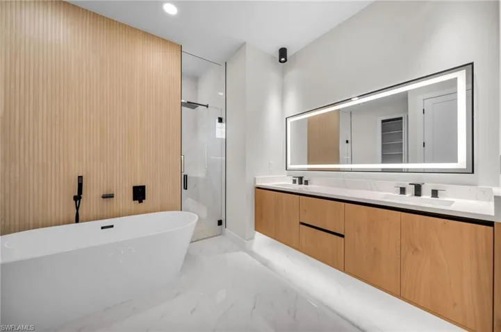 Bathroom with double vanity, marble finish floor, a freestanding tub, a sink, and a stall shower