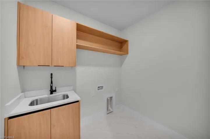 Clothes washing area with cabinet space, a sink, hookup for a washing machine, marble finish floor, and baseboards