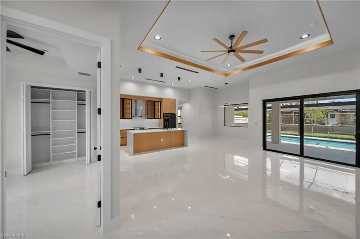 Unfurnished living room with a tray ceiling, ceiling fan, and marble finish floor