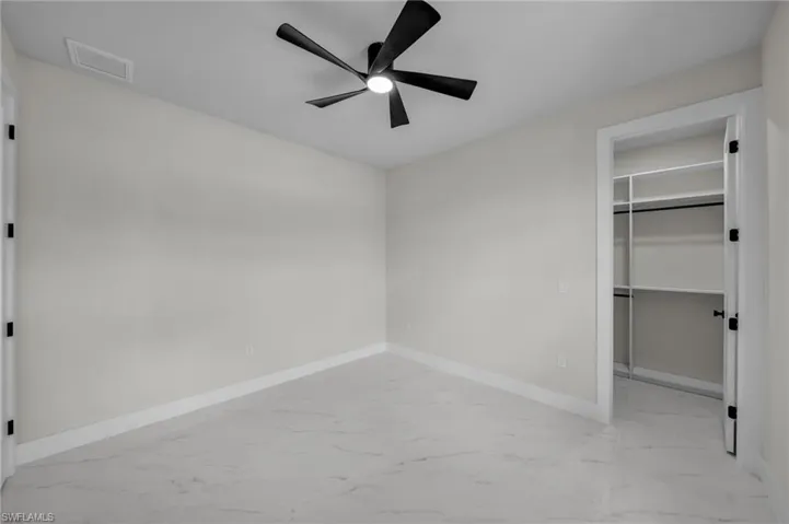 Unfurnished bedroom featuring a walk in closet, marble finish floor, baseboards, visible vents, and a closet