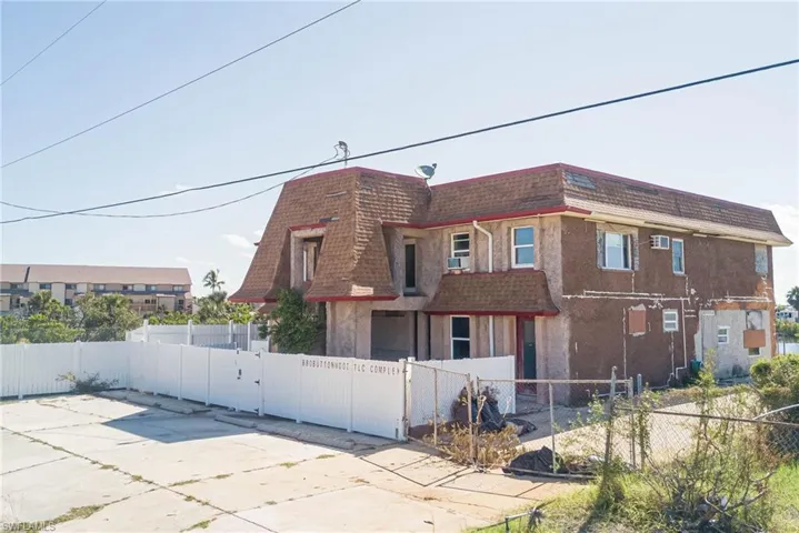 View of side of property with mansard roof, roof with shingles, a fenced front yard, and a gate