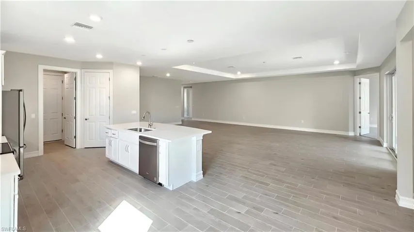 Kitchen featuring a tray ceiling, stainless steel appliances, a kitchen island with sink, and white cabinets
