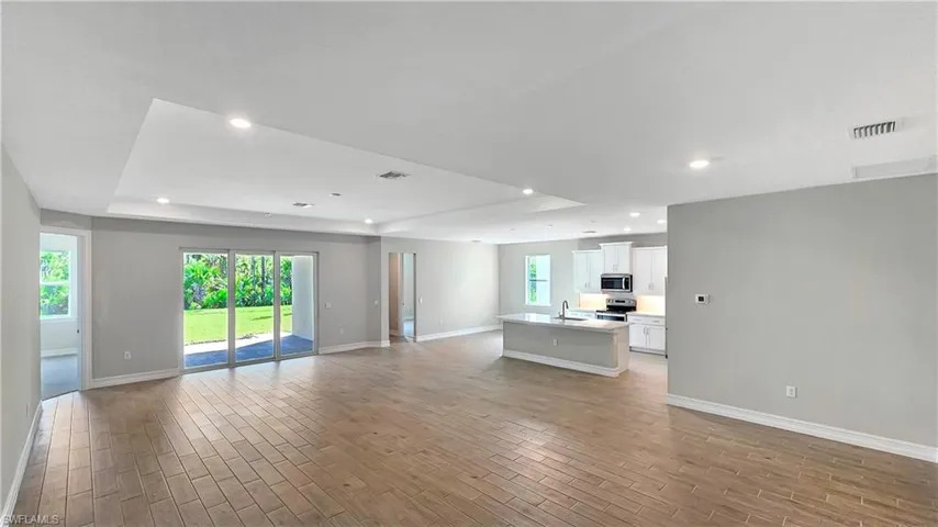 Unfurnished living room with a wealth of natural light, a raised ceiling, sink, and light hardwood / wood-style floors